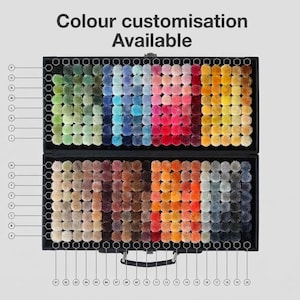 May include: A black case displaying a wide array of colorful pom-poms, arranged in rows. The pom-poms span a spectrum of colors, from greens and blues to pinks, oranges, and grays. The text "Colour Customisation Available" is at the top.