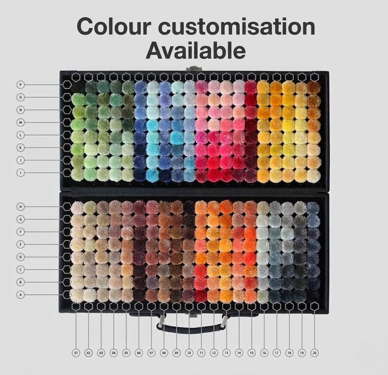 May include: A black case displaying a wide array of colorful pom-poms, arranged in rows. The pom-poms span a spectrum of colors, from greens and blues to pinks, oranges, and grays. The text "Colour Customisation Available" is at the top.