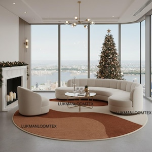 May include: A contemporary living room featuring a curved beige sofa, an armchair, and a round coffee table. A patterned rug in brown and cream tones is on the floor. A decorated Christmas tree is visible in the background.