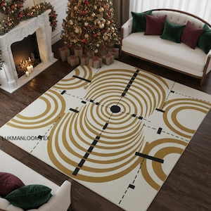 May include: A rectangular rug with a cream base and a geometric pattern in gold and black. The design includes concentric circles, straight lines, and curved shapes. The rug is on a dark wood floor in a living room setting, with a Christmas tree.