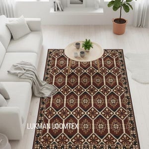 May include: A patterned rectangular rug in a living room setting. The rug features a geometric design in brown, black, and cream. The text "LUKMAN LOOMTEX" is visible on the rug. The rug is placed in a room with white furniture and a wooden coffee table.
