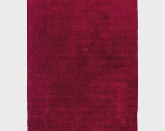 Puede incluir: Una alfombra rectangular de color burdeos oscuro con una superficie suave y texturizada. La alfombra es de un tono rojo intenso, y las fibras parecen tener un ligero brillo. La alfombra se muestra sobre un fondo blanco.