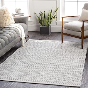 May include: A rectangular area rug with a geometric pattern in shades of gray and white. The rug features a repeating zigzag and dotted design, suitable for a living room or bedroom. The rug is placed on a dark wood floor.