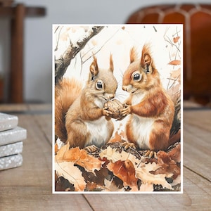 May include: Two brown squirrels sharing a walnut in a watercolor painting. The squirrels are sitting on a bed of autumn leaves.