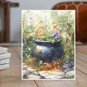May include: Watercolor painting of a black cauldron overflowing with colorful flowers. The flowers include yellow, purple, and blue blooms. The cauldron sits on a stone path with grass and other flowers surrounding it. The background is a soft green.