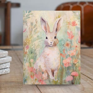 May include: A watercolor painting of a white rabbit with pink ears and a long nose standing in a field of pink and green flowers.