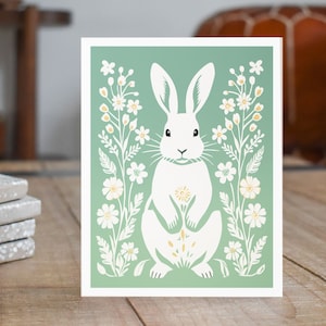 May include: A white rabbit with long ears sits in a field of white flowers with yellow centers. The background is a light green color.