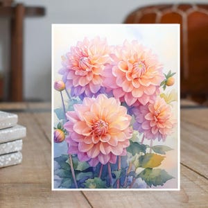 May include: A watercolor painting of several dahlias in shades of pink and peach. The flowers have multiple layers of petals and are surrounded by green leaves and buds. The artwork is on a white background.