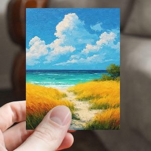 May include: A small, rectangular painting depicts a beach scene. The sky is a bright blue with fluffy white clouds. The ocean is turquoise and dark blue. Golden yellow grass lines a sandy path leading to the water.