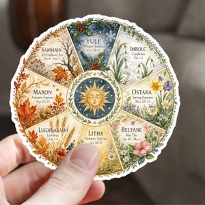 May include: A circular sticker featuring a watercolor illustration of the Wheel of the Year. The design includes eight sections representing seasonal festivals like Samhain, Yule, and Litha, with corresponding dates and imagery of leaves, flowers, and snowflakes.