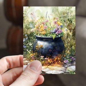 May include: Watercolor painting of a black cauldron overflowing with colorful flowers. The flowers include yellow, pink, and purple blooms. The cauldron sits on a stone path, with a soft, glowing light emanating from beneath it. The background features lush greenery.