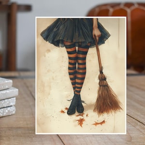 May include: A watercolor painting of a witch with black and orange striped stockings and a black skirt standing next to a broom. The witch is standing on a light brown background with fallen leaves.