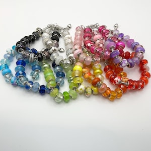 May include: A collection of multiple charm bracelets featuring a variety of colorful glass beads in shades of blue, green, yellow, orange, red, pink, and purple, interspersed with silver-toned metal spacers and small heart-shaped charms.