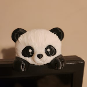 Puede incluir: Una figura de oso panda impresa en 3D en blanco y negro. El panda tiene orejas, ojos y patas negras, con cara y cuerpo blancos. La figura está posada sobre una superficie negra.