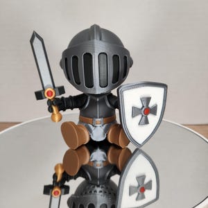 May include: A 3D-printed knight figurine with a gray helmet, armor, and a shield. The shield features a white background with a red cross. The knight holds a silver sword with a red accent. The figurine is brown and gray.