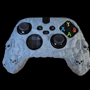 Könnte beinhalten: Ein grauer und schwarzer Xbox-Controller mit einem Totenkopf-Design. Der Controller hat eine strukturierte Oberfläche und ist für Spiele konzipiert.