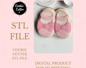 May include: A pair of baby shoe cookies with pink bows and straps. The cookies are on a white surface, with the text "STL FILE" and "DIGITAL PRODUCT FOR 3D PRINTING" in the background. The image also includes the text "COOKIE CUTTER STL FILE".