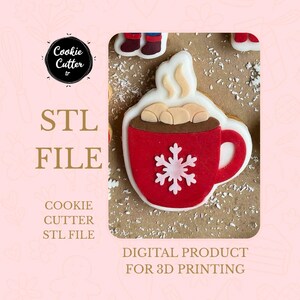 Op de afbeelding: Een rode koekjesvorm in de vorm van een warme chocolademok met een witte sneeuwvlok. De koek heeft witte glazuur en marshmallows. De afbeelding bevat de tekst "STL FILE" en "DIGITAL PRODUCT FOR 3D PRINTING".