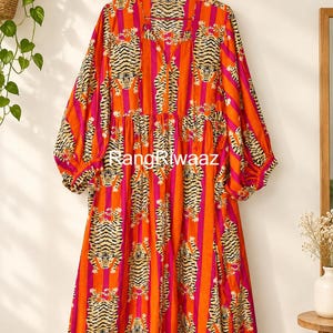 May include: A long-sleeved midi dress featuring a vibrant orange and magenta vertical striped pattern with a repeating tiger print. The dress has a V-neckline with a tie closure, gathered waist, and voluminous sleeves. The text RangRiwaaz is visible.