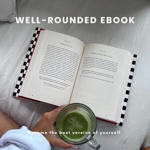 Peut inclure: Un livre ouvert avec le titre "Well-Rounded Ebook" sur une surface blanche. Le livre est ouvert à deux pages avec le texte "Narking Personal" et "Everyone Wants More Power". Une personne tient un verre de liquide vert.