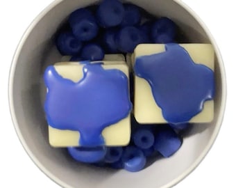 May include: Two white wax melts with a blue wax topping in a white bowl with blue wax beads.