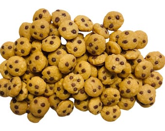 Puede incluir: Un montón de galletas pequeñas y redondas de color marrón claro con chispas de chocolate oscuro. Las galletas están dispersas, creando una superficie texturizada. La imagen está bien iluminada, resaltando los detalles de cada galleta.