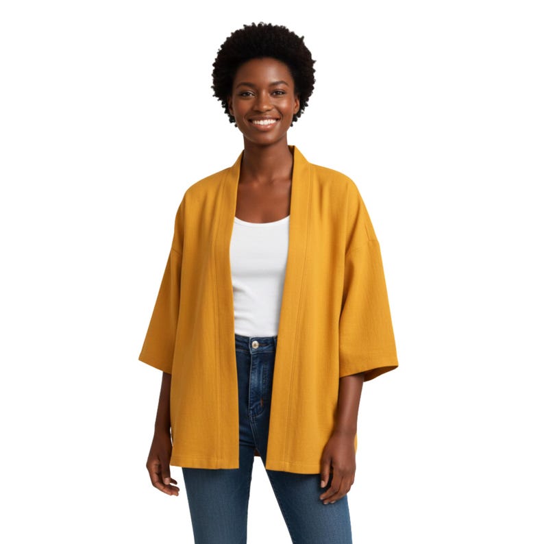 May include: Mustard yellow kimono-style jacket with three-quarter sleeves. The open-front cardigan is paired with a white top and blue jeans. The jacket has a relaxed fit and a textured appearance.