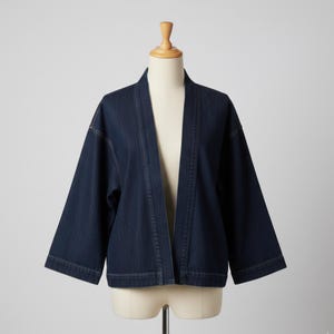 May include: A dark blue denim jacket with a kimono-style design. The jacket features a collarless neckline, three-quarter sleeves, and a straight hem. The garment is displayed on a mannequin against a plain white background.