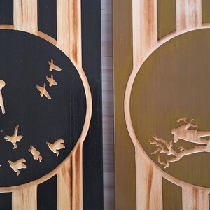 May include: Two wooden panels with carved designs. One panel features a black circle with flying bird silhouettes. The other panel has a gold circle with a tree and deer carving. The panels have vertical wood grain.
