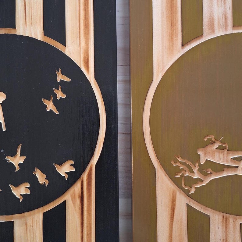 May include: Two wooden panels with carved designs. One panel features a black circle with flying bird silhouettes. The other panel has a gold circle with a tree and deer carving. The panels have vertical wood grain.