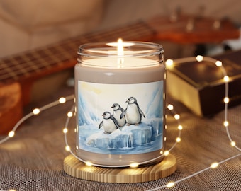 May include: A brown candle with a white wax top and a printed image of three penguins on an iceberg. The candle is on a wooden base and surrounded by white fairy lights.