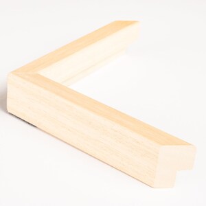 May include: A close-up of a corner of a natural wood picture frame. The frame is made of a light, unfinished wood with a smooth surface.