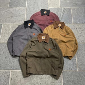 Pode incluir: Quatro jaquetas com fecho de correr em bordô, cinzento, castanho claro e verde azeitona. Cada jaqueta apresenta uma gola contrastante, um fecho frontal completo, dois bolsos inferiores e um pequeno bolso no peito com o logótipo Carhartt.