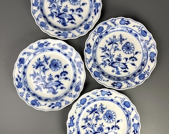 Op de afbeelding: Vier witte keramische borden met een blauw bloemmotief. Elk bord heeft een geschulpte rand en een gedetailleerd patroon van bloemen, bladeren en vogels. De borden zijn gerangschikt op een grijze ondergrond.
