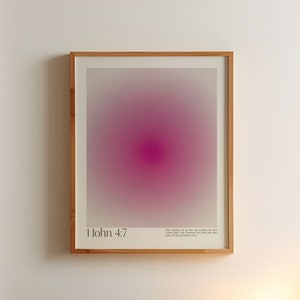 Puede incluir: Una impresión enmarcada con un diseño degradado en rosa y blanco. La impresión tiene el texto "1 Juan 4:7" y un versículo bíblico debajo. La impresión está colgada en una pared blanca sobre una cama con una manta marrón y una mesita de noche con una lámpara.