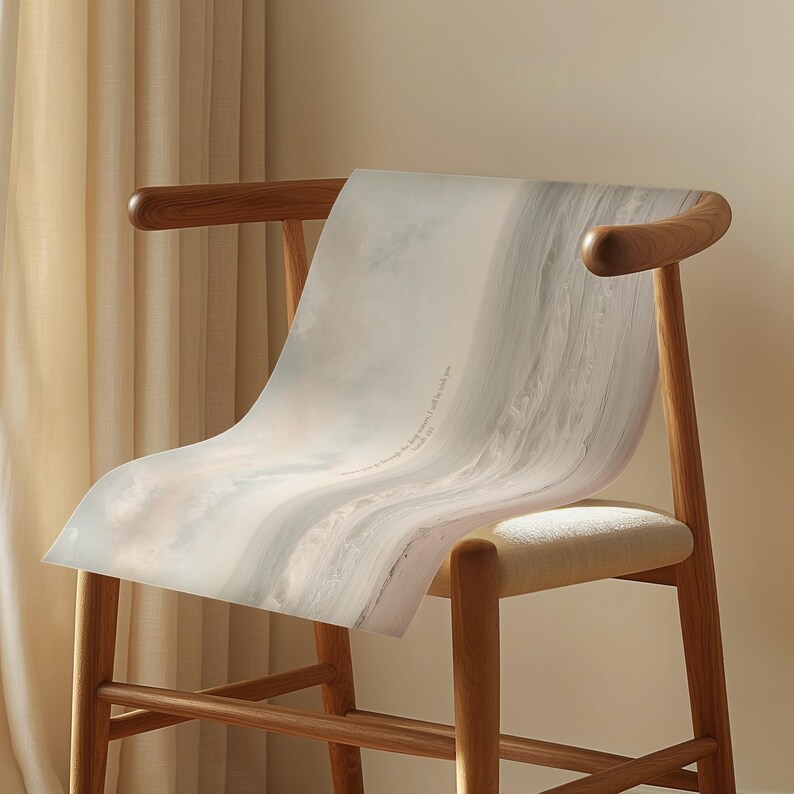 May include: A wooden chair with a light-colored woven seat and curved back. A large, light-colored print with a cloudy, abstract design is draped over the chair. The print has text that reads "If you walk through the fire, I will be with you."
