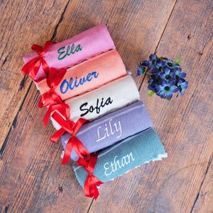 Five rolled Turkish beach towels in various colors with personalized name embroidery. Each towel is tied with a red ribbon, perfect for personalized gifts, bachelorette parties, and custom events.