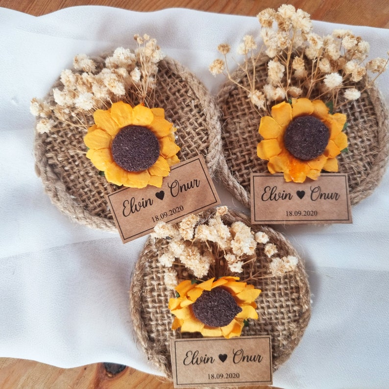 May include: Three round burlap and twine ornaments with a dried flower arrangement and a sunflower in the center. Each ornament has a brown paper tag with the text "Elvin &hearts; Onur 18.09.2020".