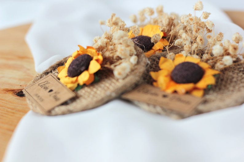 May include: Three small burlap and dried flower arrangements with a sunflower and a tag that says "Ellen & Paul" with a heart and the date "08.27.23".