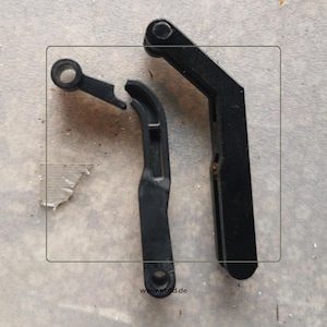 Puede incluir: Tres piezas de máquina de plástico negro están dispuestas sobre una superficie gris. Una pieza está rota. Las piezas tienen varias formas, incluyendo una pieza curva, una pieza con un agujero y una pieza larga y angular. El sitio web www.pbsd.de es visible.