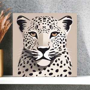 May include: Square canvas art featuring a stylized leopard portrait. The artwork showcases a beige background with a leopard's face in shades of black, white, and tan. The leopard has black spots and tan eyes. The art is displayed on a white shelf.
