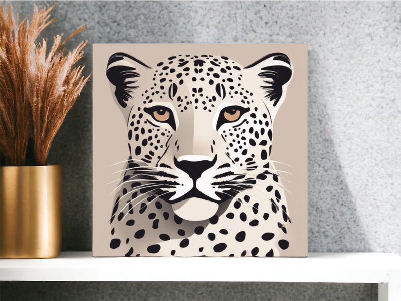 May include: Square canvas art featuring a stylized leopard portrait. The artwork showcases a beige background with a leopard's face in shades of black, white, and tan. The leopard has black spots and tan eyes. The art is displayed on a white shelf.