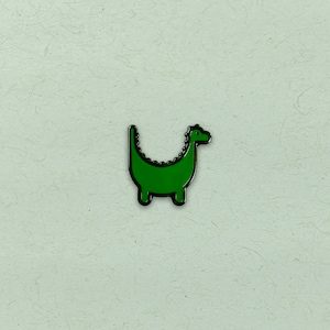 May include: A green enamel pin shaped like a dinosaur with a long neck and a small head.