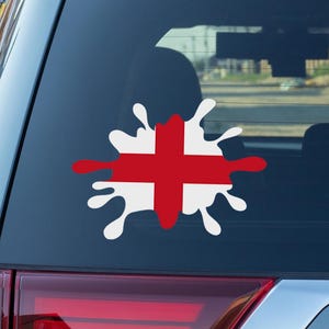 May include: A car window decal featuring the English flag in a splash design. The flag is red and white, with a red cross on a white background. The decal is applied to the rear window of a gray SUV.