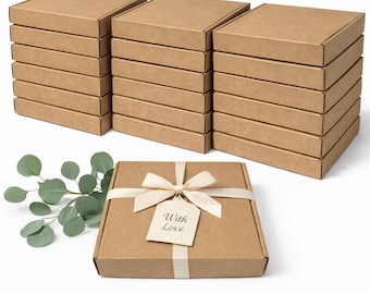 May include: Several stacks of brown cardboard boxes with lids. One box is decorated with a cream-colored ribbon, bow, and a tag that reads "With Love". A sprig of green eucalyptus is on the left side of the box.