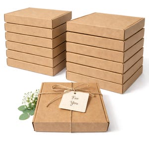 Può includere: Pile di scatole quadrate di cartone marrone con coperchi. Una scatola è legata con spago e un'etichetta che dice "For You". Foglie verdi e fiori bianchi sono sul lato della scatola legata. Le scatole sono su sfondo bianco.
