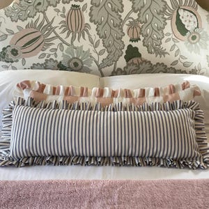 Navy and pink striped lumbar cushions sitting atop a bed with a pink bedspread and a floral headboard