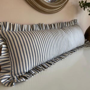 A long, white and blue striped bolster cushion with a frilled edge. The cushion is made of a soft, comfortable fabric and is perfect for adding a touch of style to any room.