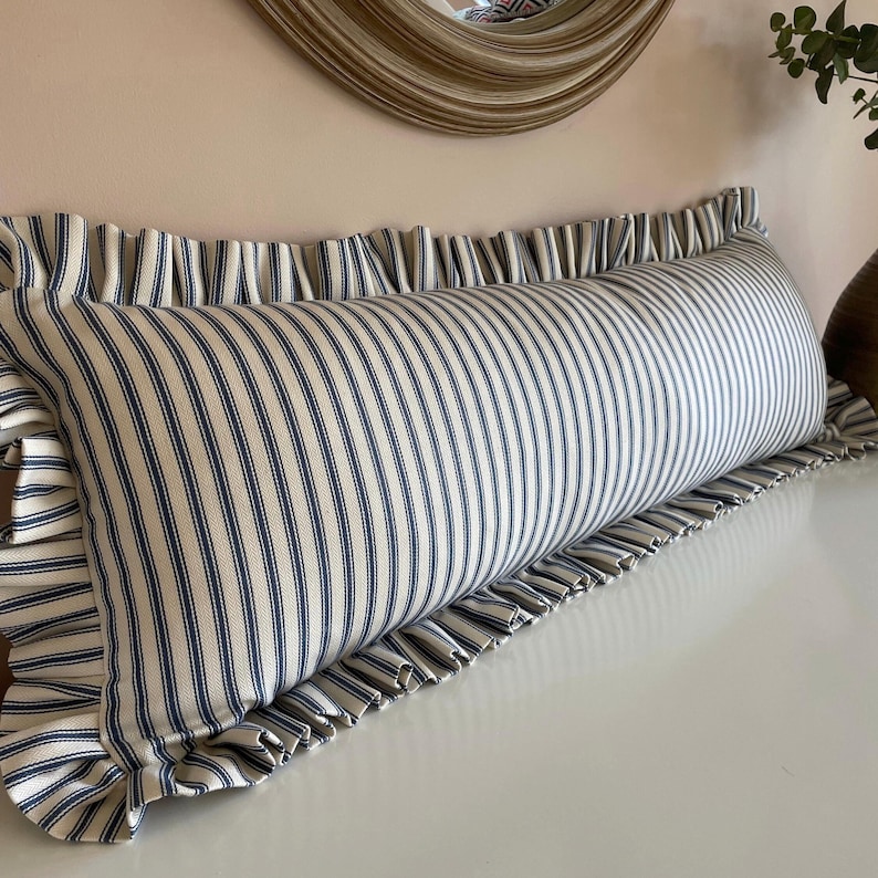 A long, white and blue striped bolster cushion with a frilled edge. The cushion is made of a soft, comfortable fabric and is perfect for adding a touch of style to any room.