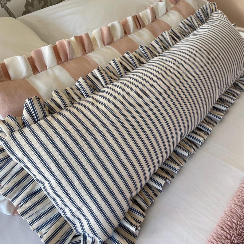 Navy and pink striped lumbar cushions sitting on a bed with white sheets and a pink bedspread